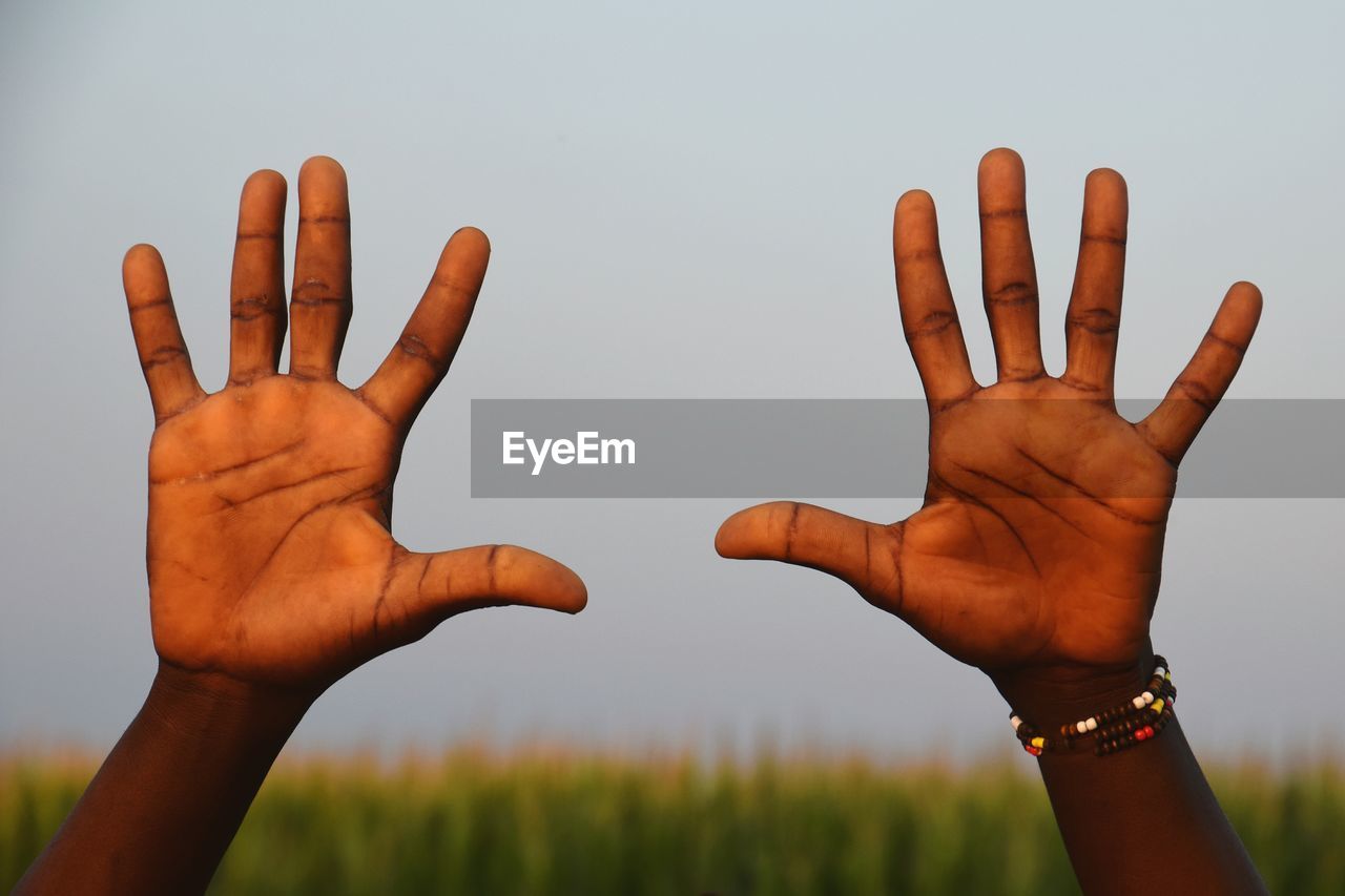 Cropped hands of person showing stop gesture against sky