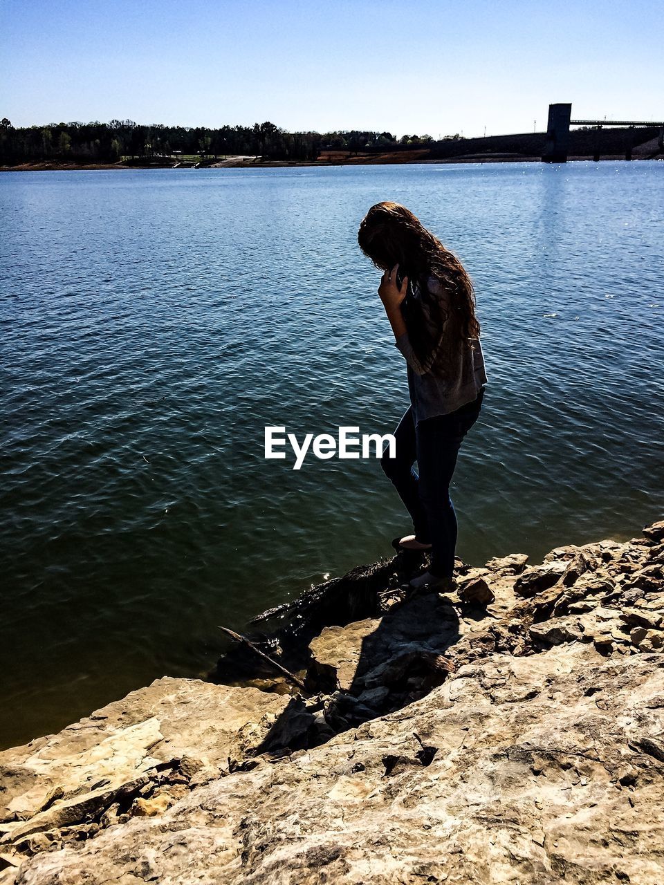 Full length side view of teenage girl standing on rock formation at riverbank