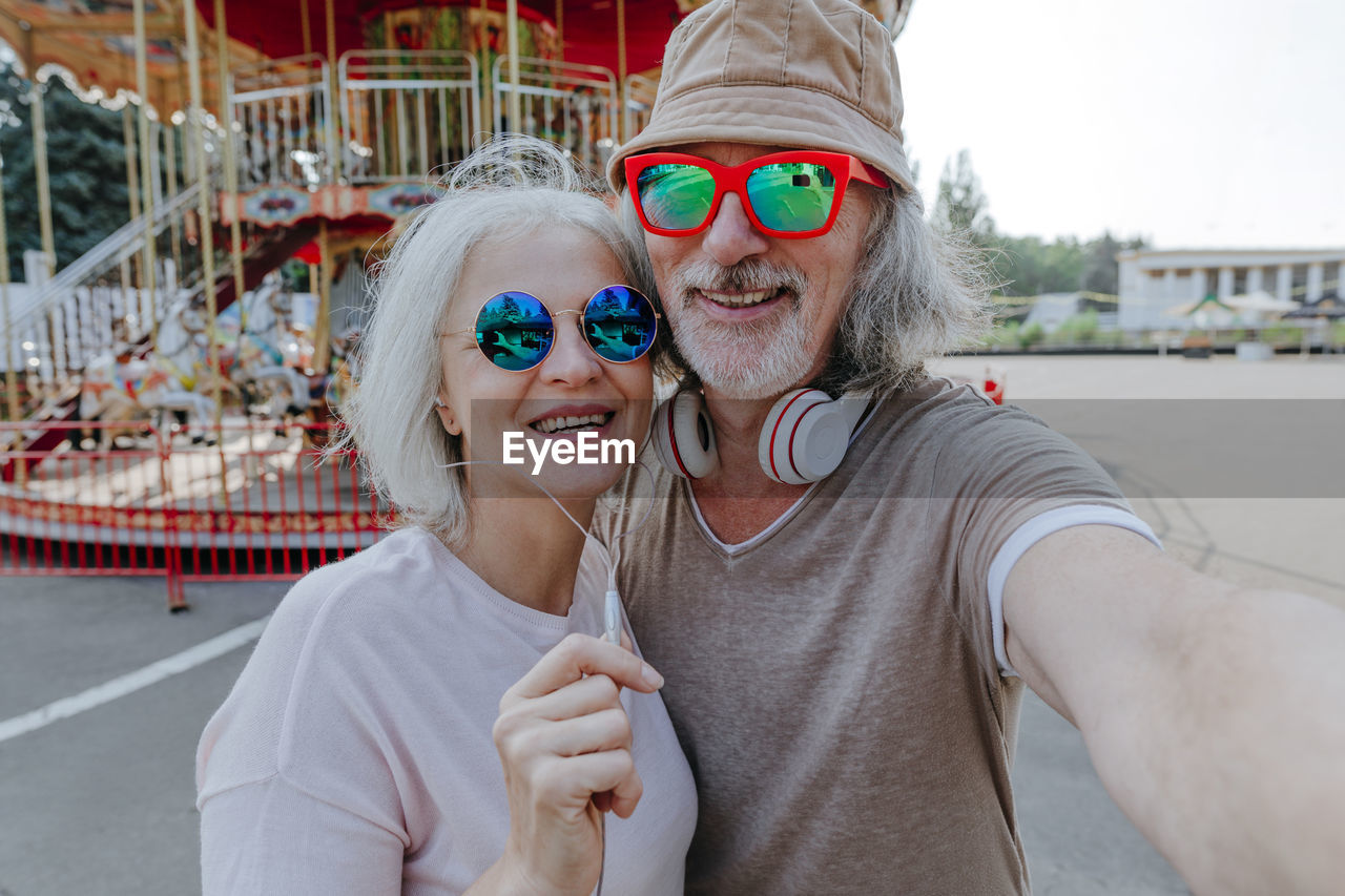 Happy couple wearing sunglasses taking selfie in amusement park