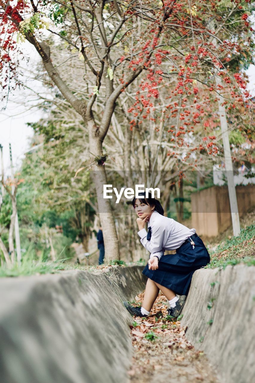 Portrait of young woman sitting against plants in park