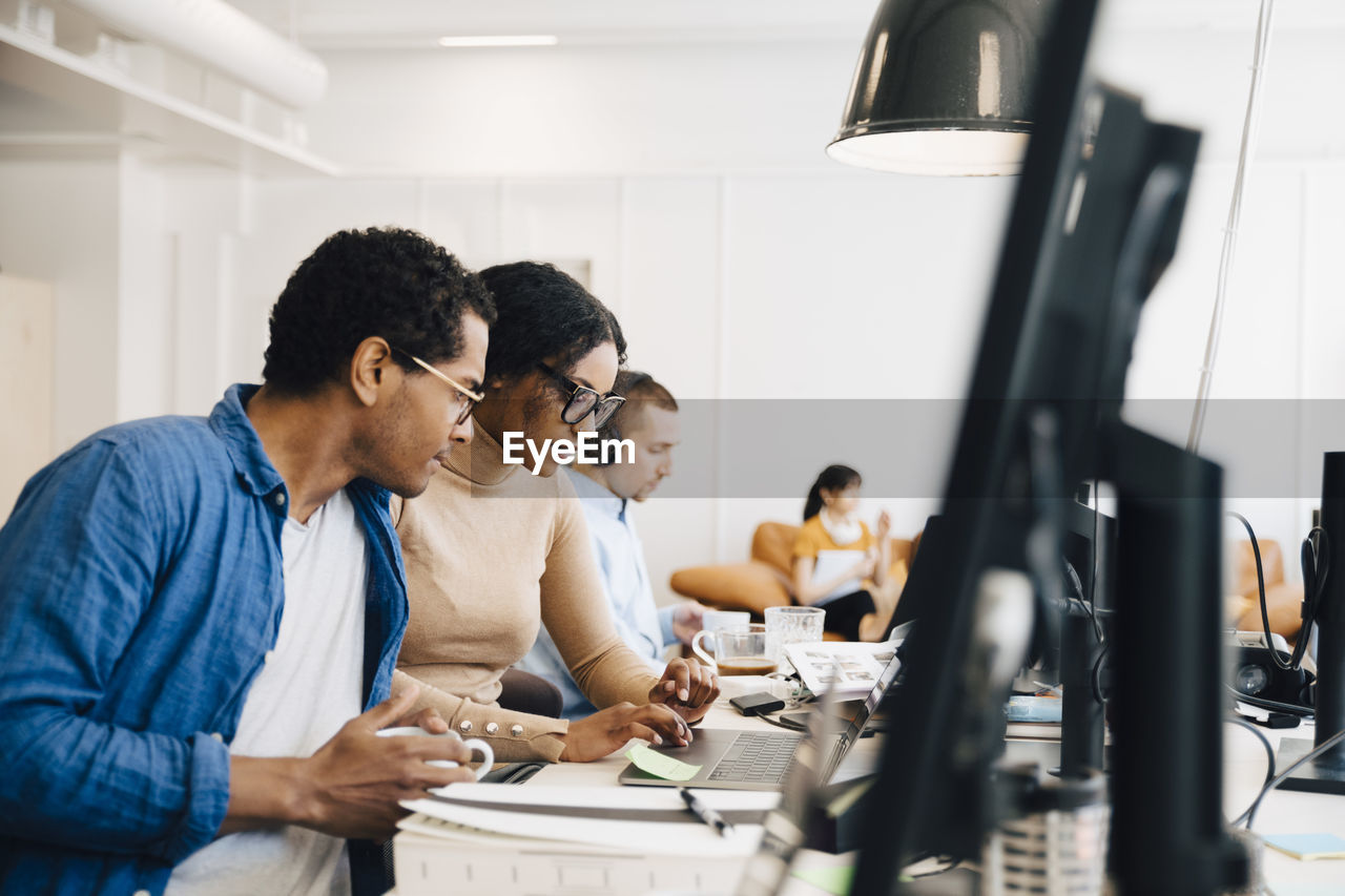 It professionals discussing over laptop on desk while sitting creative office