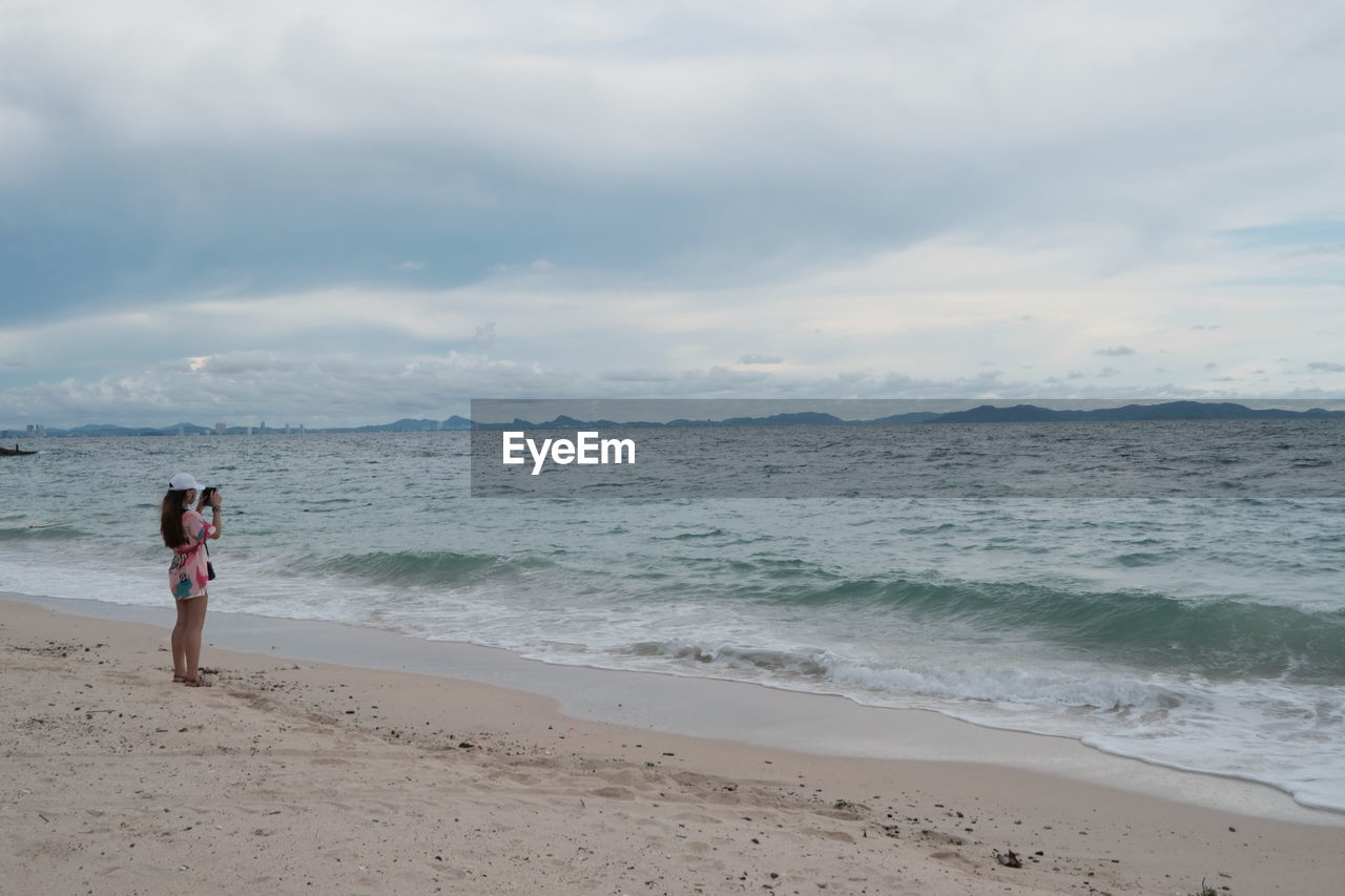 WOMAN STANDING ON BEACH AGAINST SEA