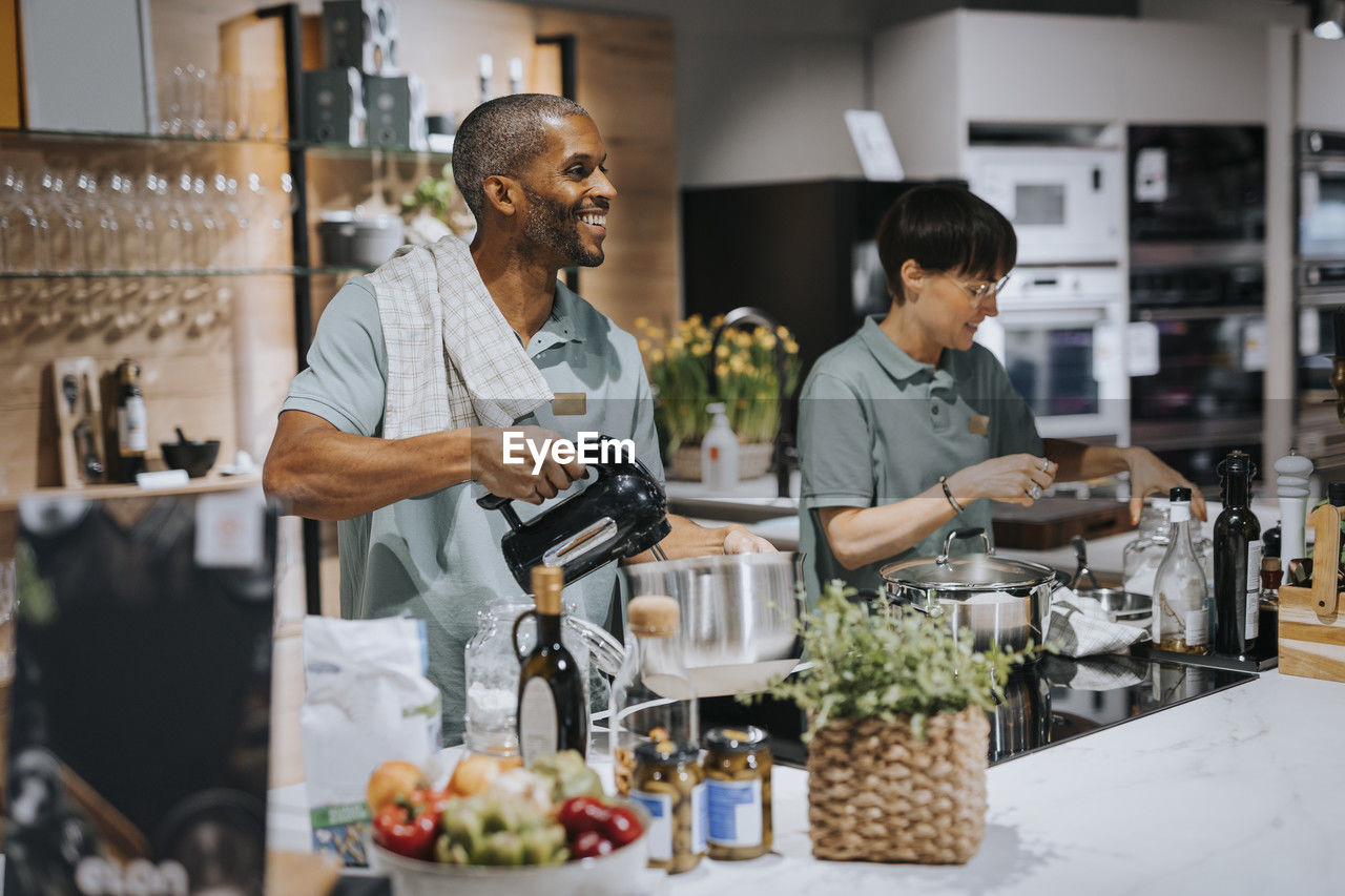 Multiracial male and female colleagues using modern kitchen appliances at store