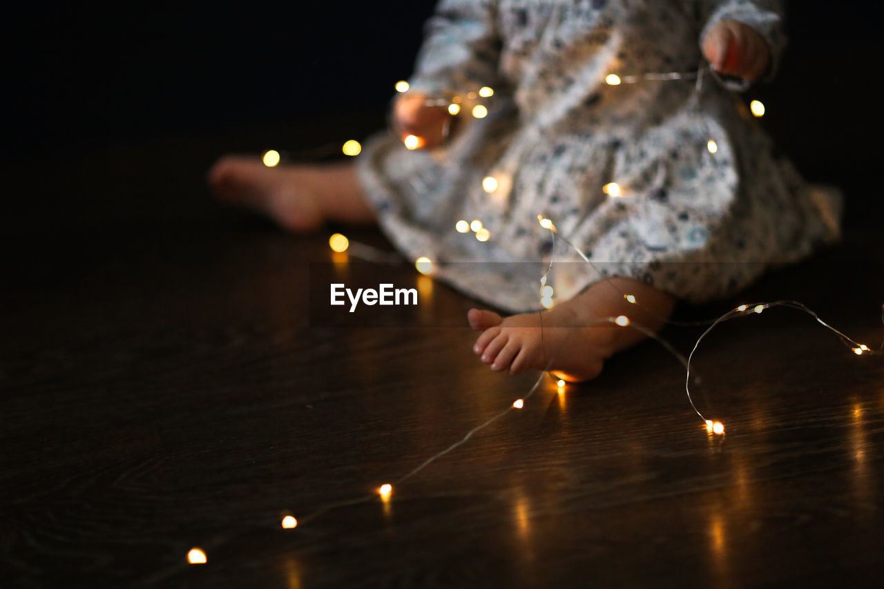 Lonely kid plays with an electric garland, cozy feet on the floor. children's safety  