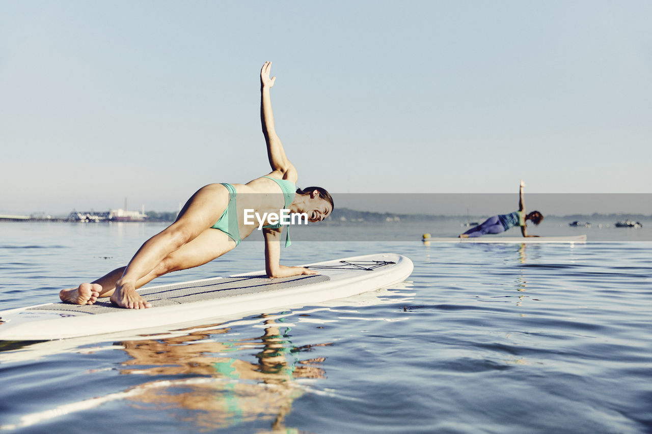 Two women on standup paddle boarders doing yoga at sunrise in the fog