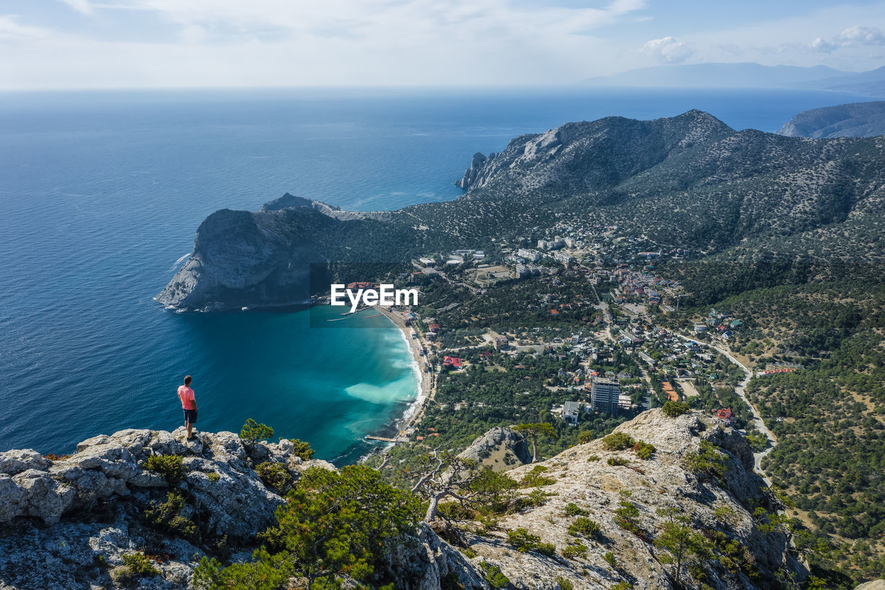 Man traveller at the top of falcon sokol mountain enjoying novyi svit town below. crimea