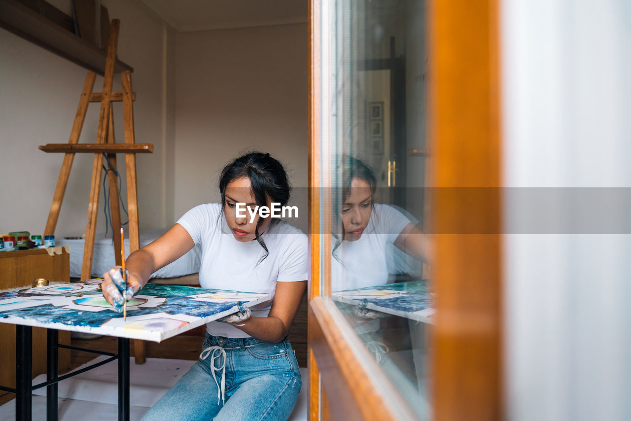 Female painter in white shirt drawing lines on easel in light studio