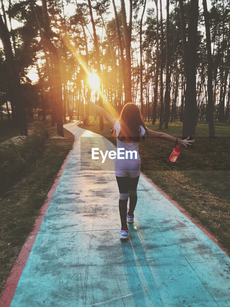 REAR VIEW OF WOMAN WALKING ON FOOTPATH AMIDST TREES