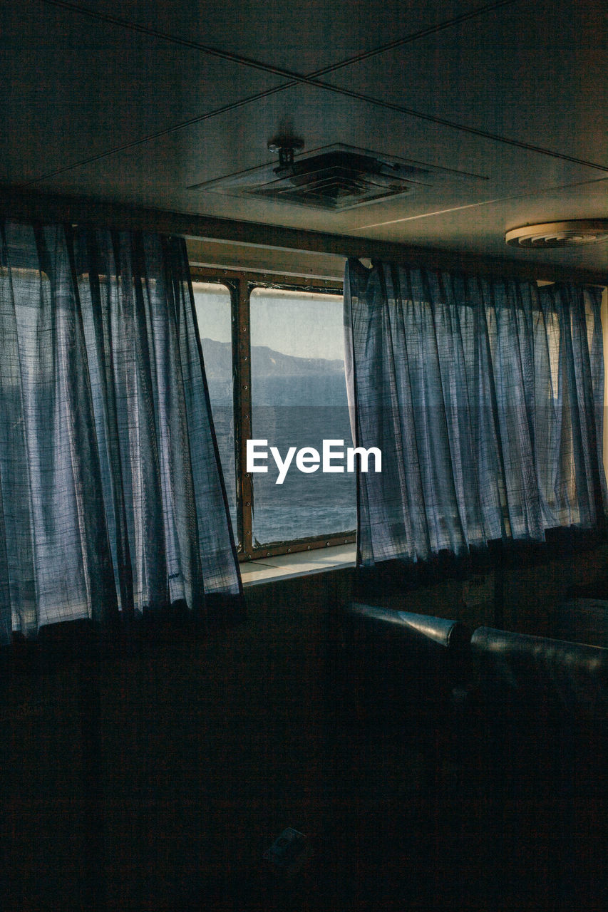 The passenger seats on the ferry boat, view through the window and curtains  behind which is sea.