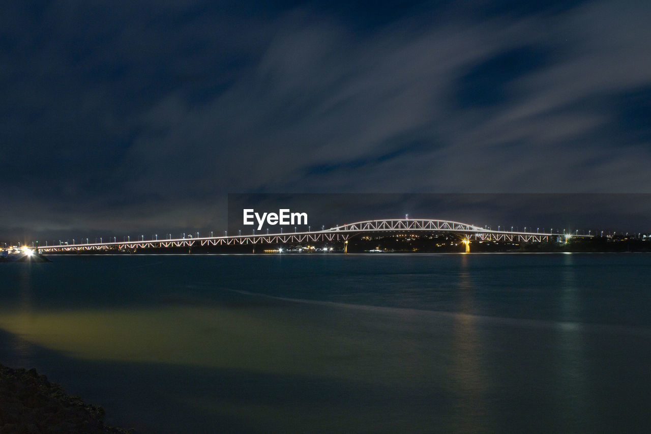 Illuminated city by sea against sky at night