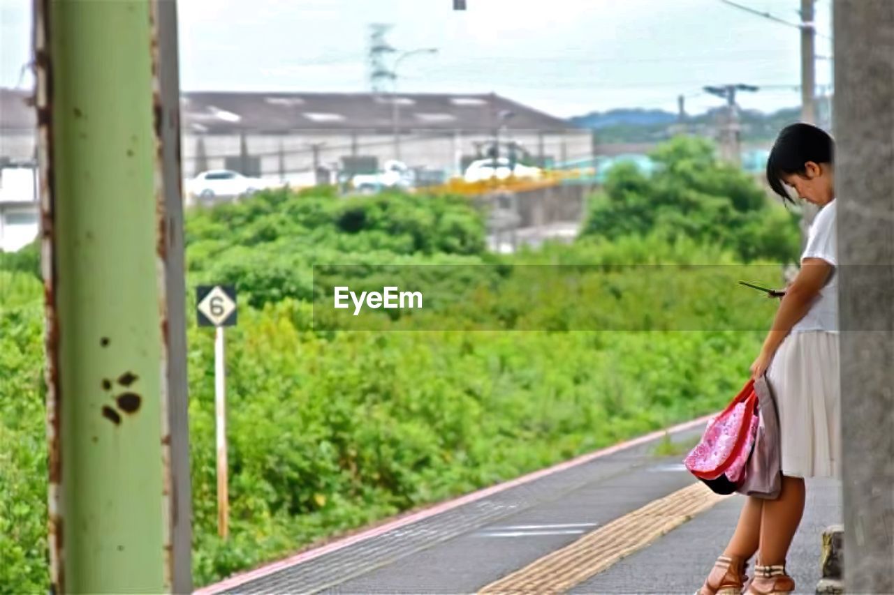 SIDE VIEW OF WOMAN WITH UMBRELLA WALKING ON RAILWAY STATION