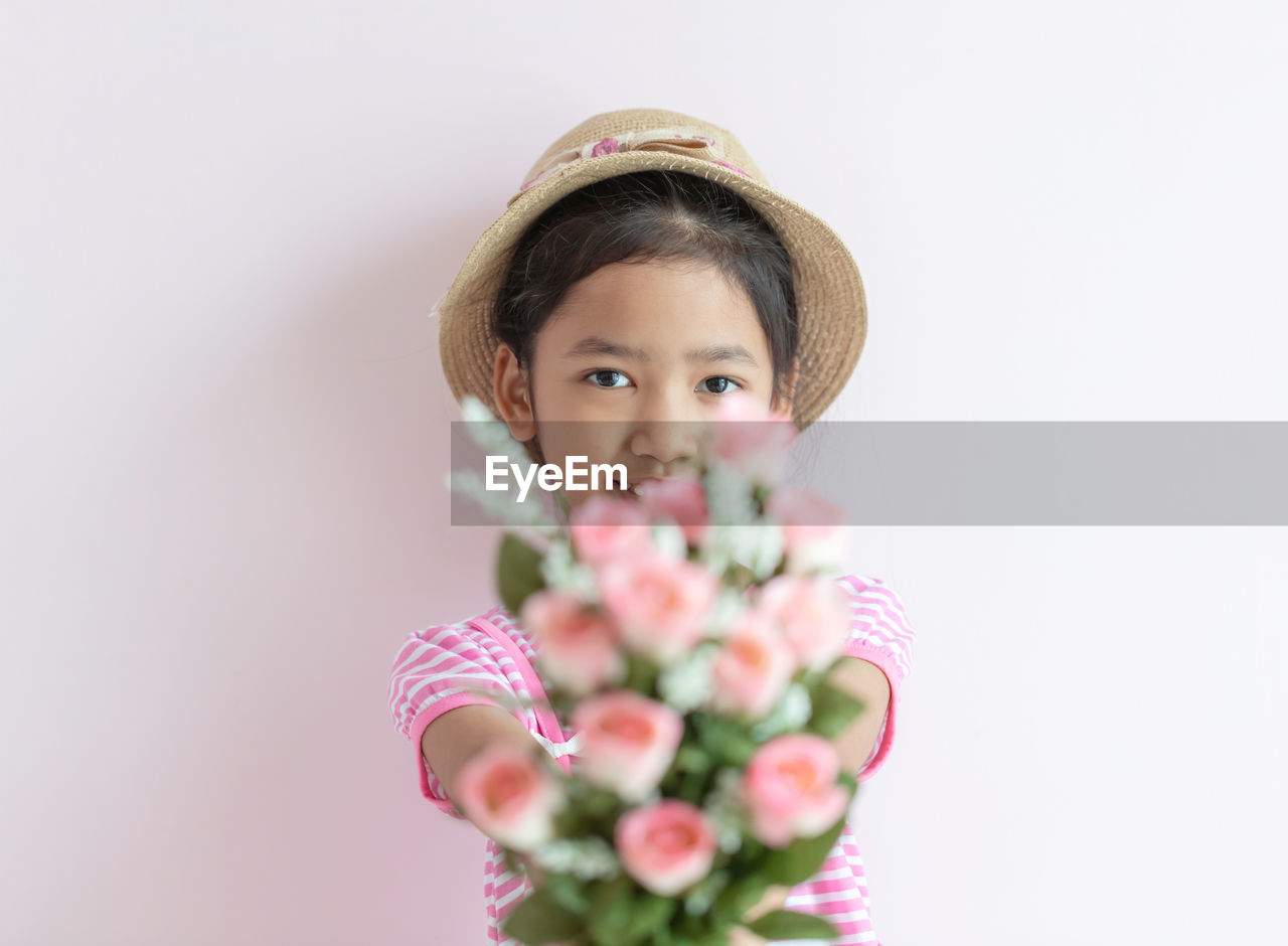 Portrait of smiling girl with pink flowers against white wall