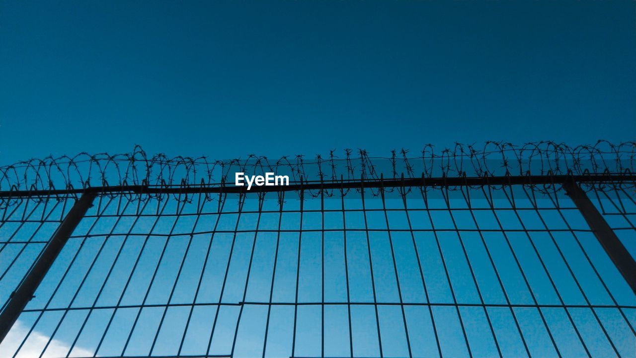 LOW ANGLE VIEW OF BARBED WIRE AGAINST CLEAR BLUE SKY