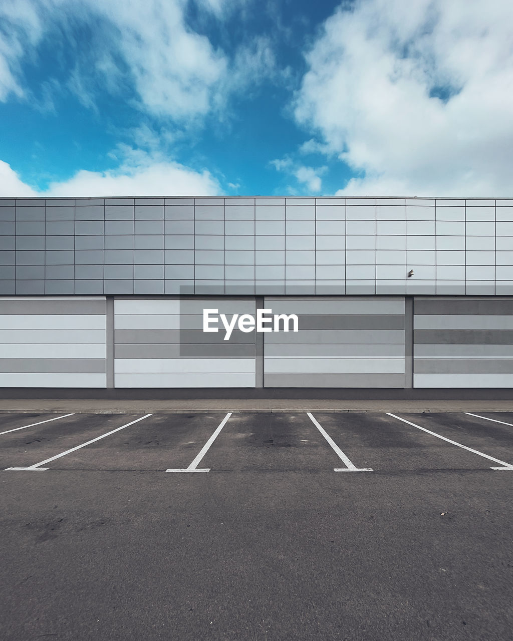 Wall of a building with an empty parking lot against a blue sky.