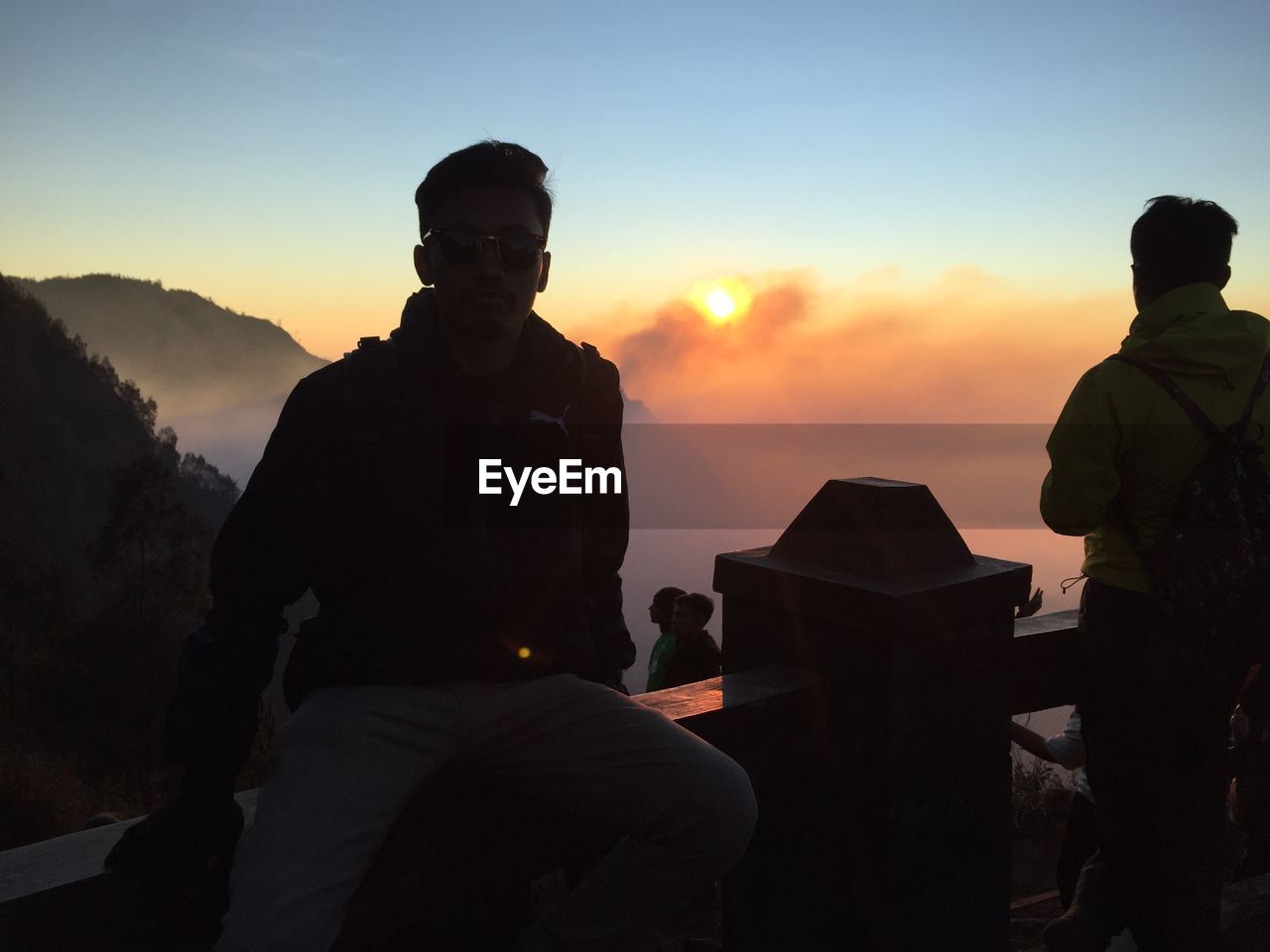 REAR VIEW OF SILHOUETTE PEOPLE STANDING ON MOUNTAIN AGAINST SKY DURING SUNSET