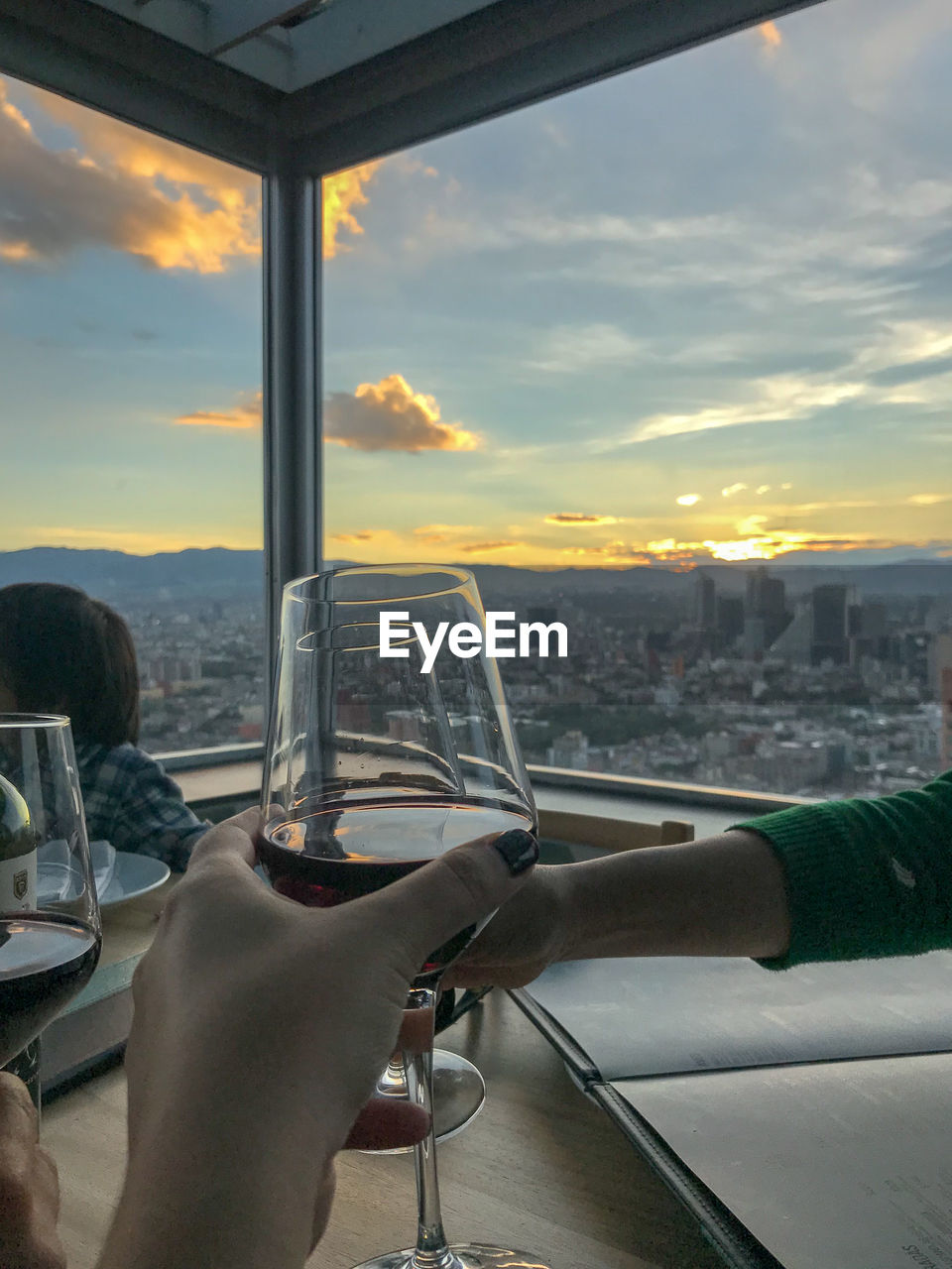 HAND HOLDING GLASS AGAINST CITYSCAPE DURING SUNSET