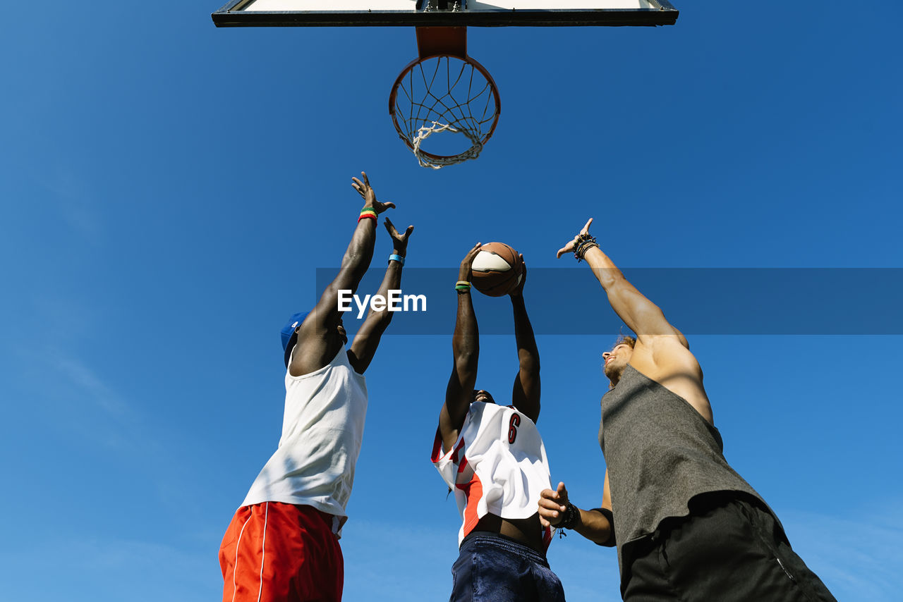 Low angle view of basketball hoop and men against blue sky