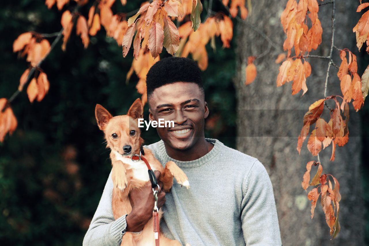 Portrait of smiling man with dog against autumn leaves