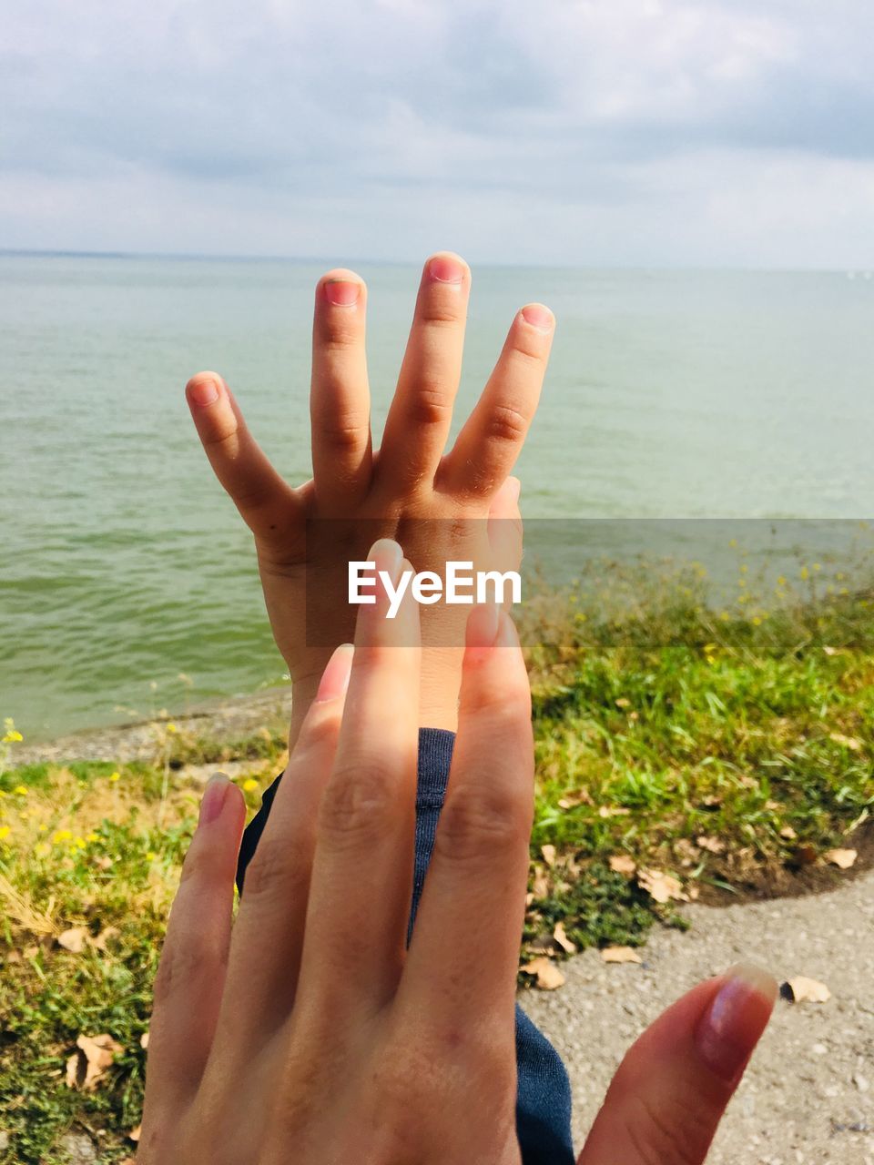 CROPPED IMAGE OF HAND AGAINST SEA