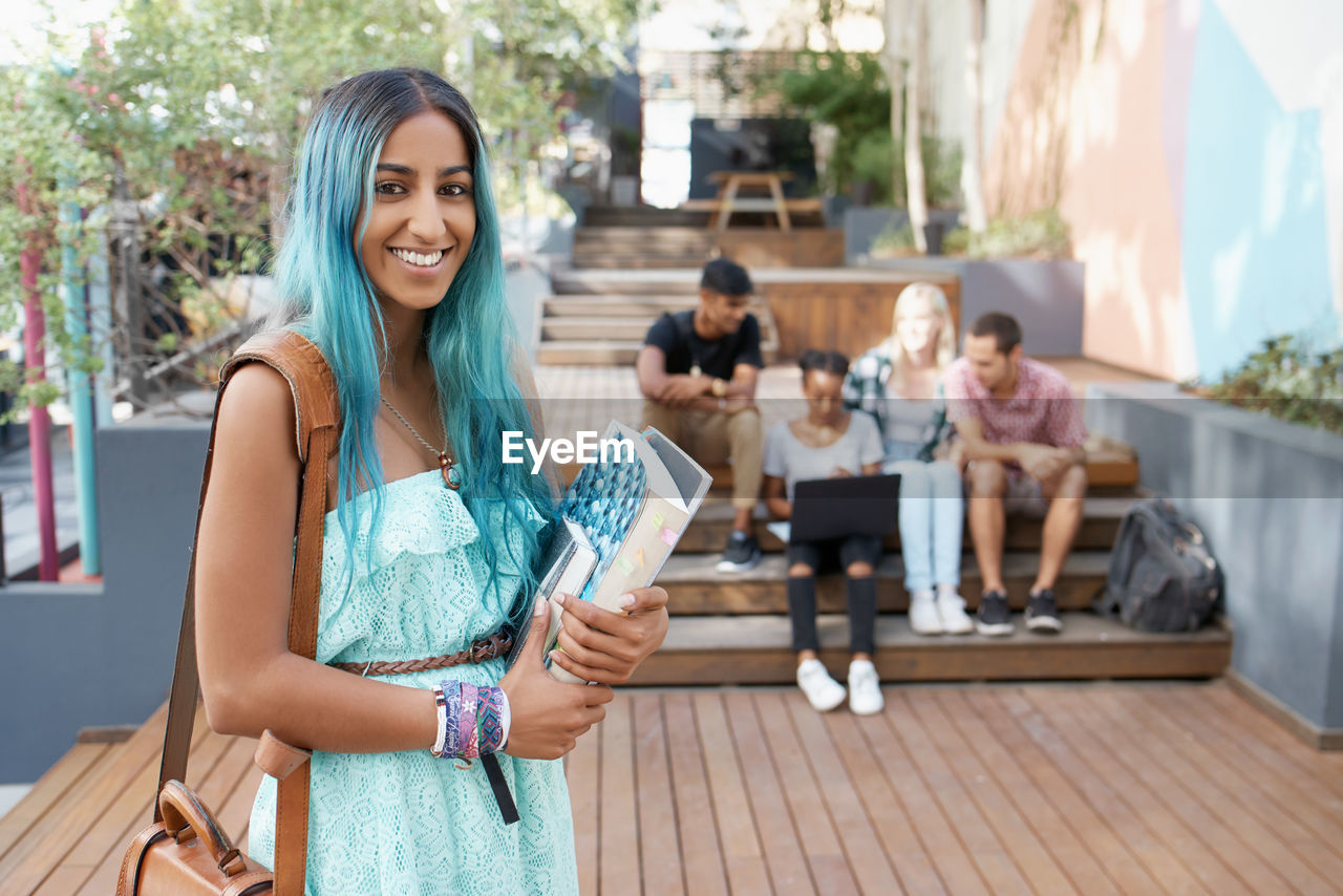 Portrait of young woman holding book with friends in background