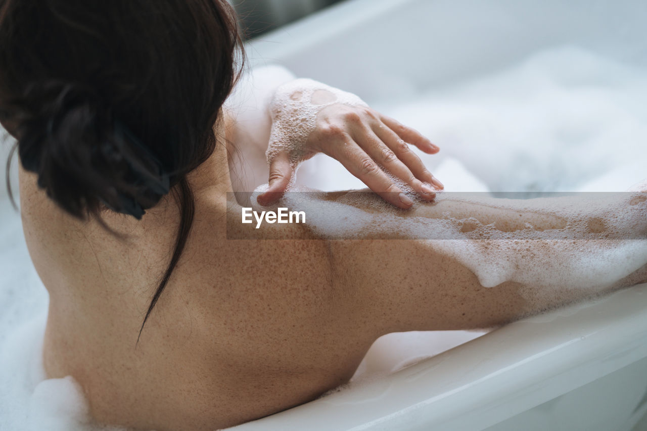 Crop photo of self loving adult brunette woman taking bath with foam at home