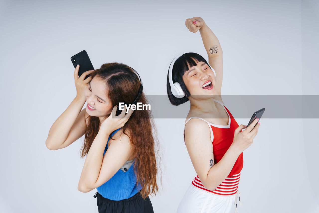 Lesbian couple using phone while listening music against gray background