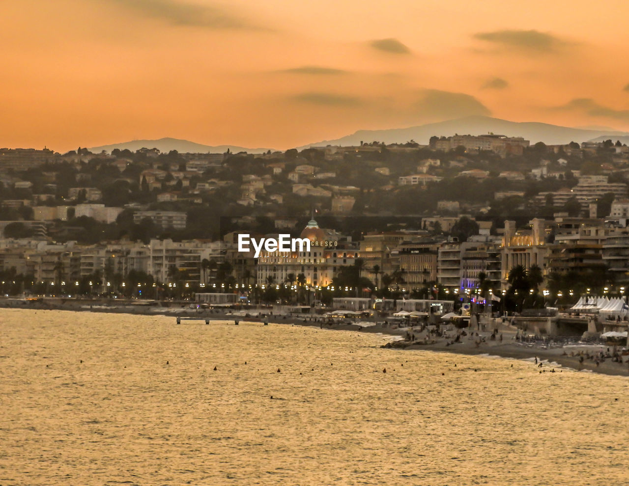 Town by sea against sky during sunset