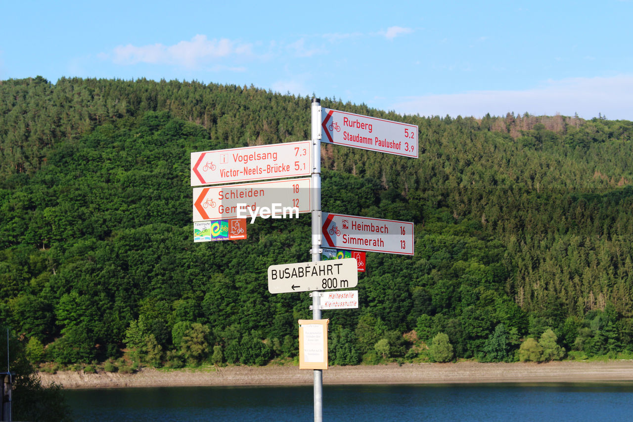 Information sign by trees against sky