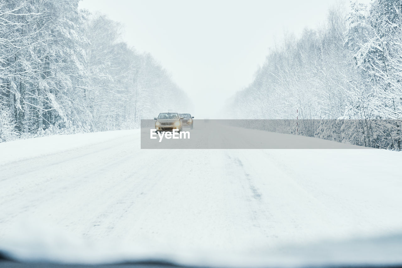 Snowy road in winter forest with moving car