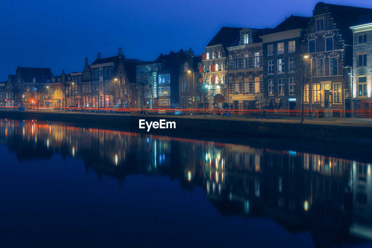 Illuminated buildings by lake against sky at night