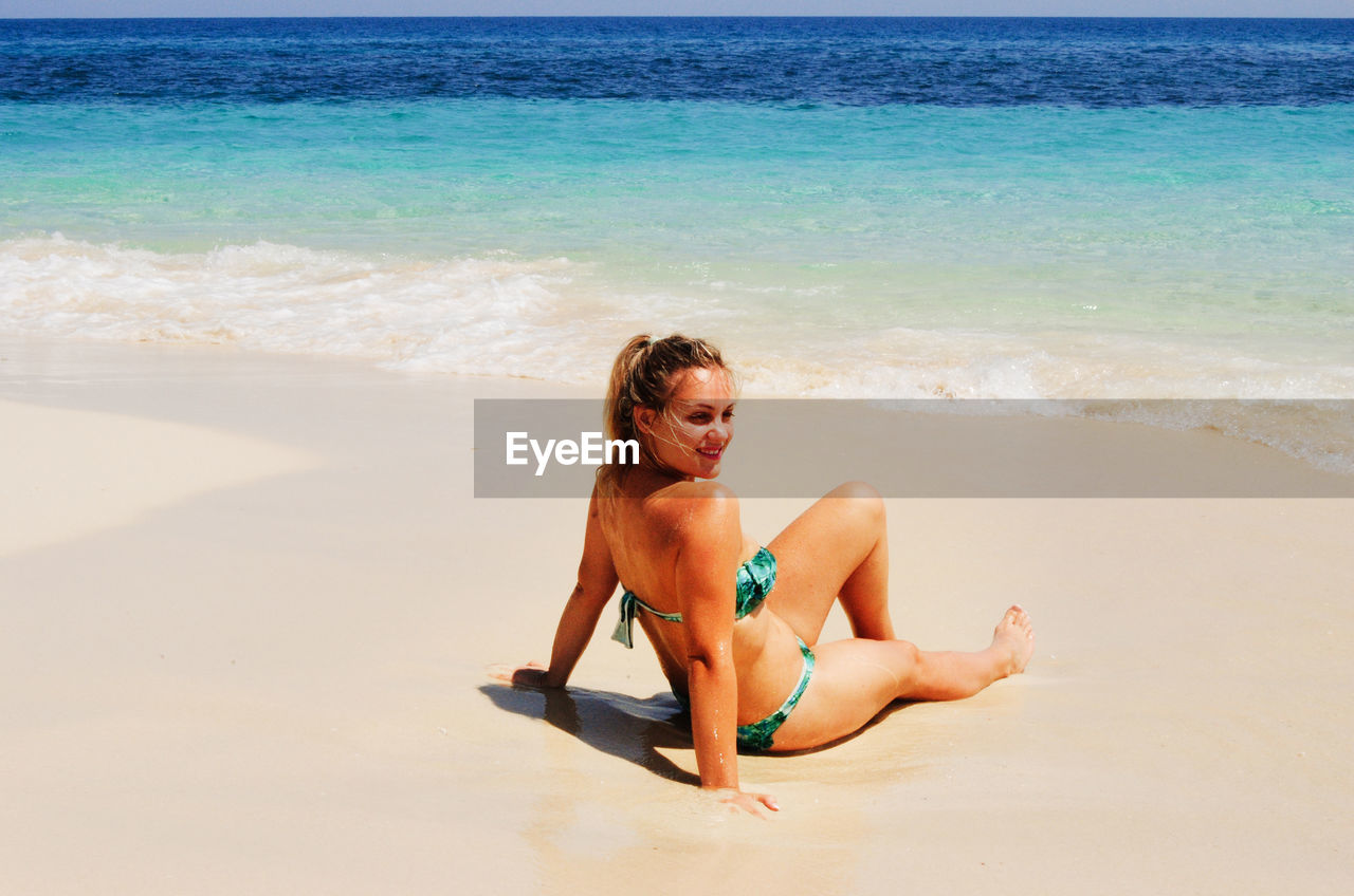 Smiling blonde woman sitting on tropical beach