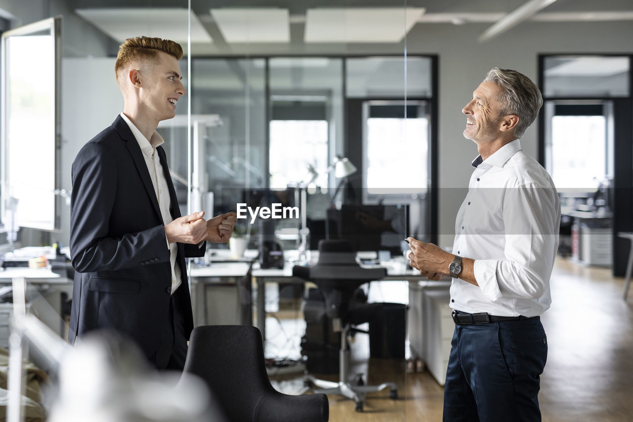 Smiling businessmen discussing while standing at open plan office