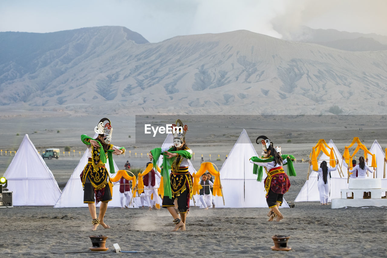 People wearing traditional clothing while dancing at desert against mountains