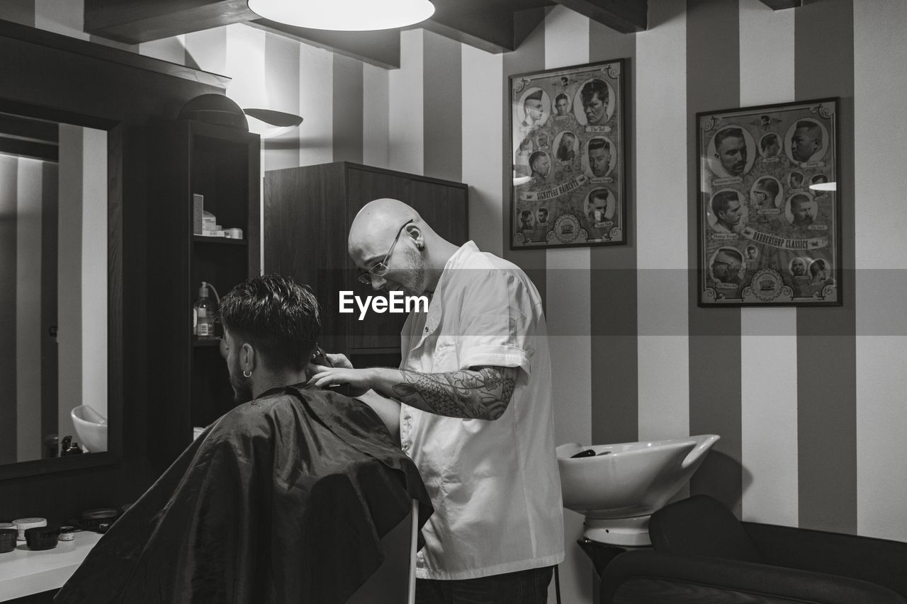 Side view of barber cutting man hair in salon