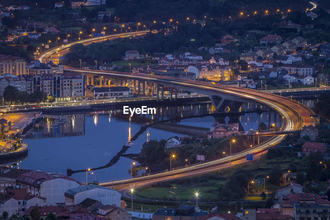 HIGH ANGLE VIEW OF ILLUMINATED BRIDGE OVER RIVER AND BUILDINGS