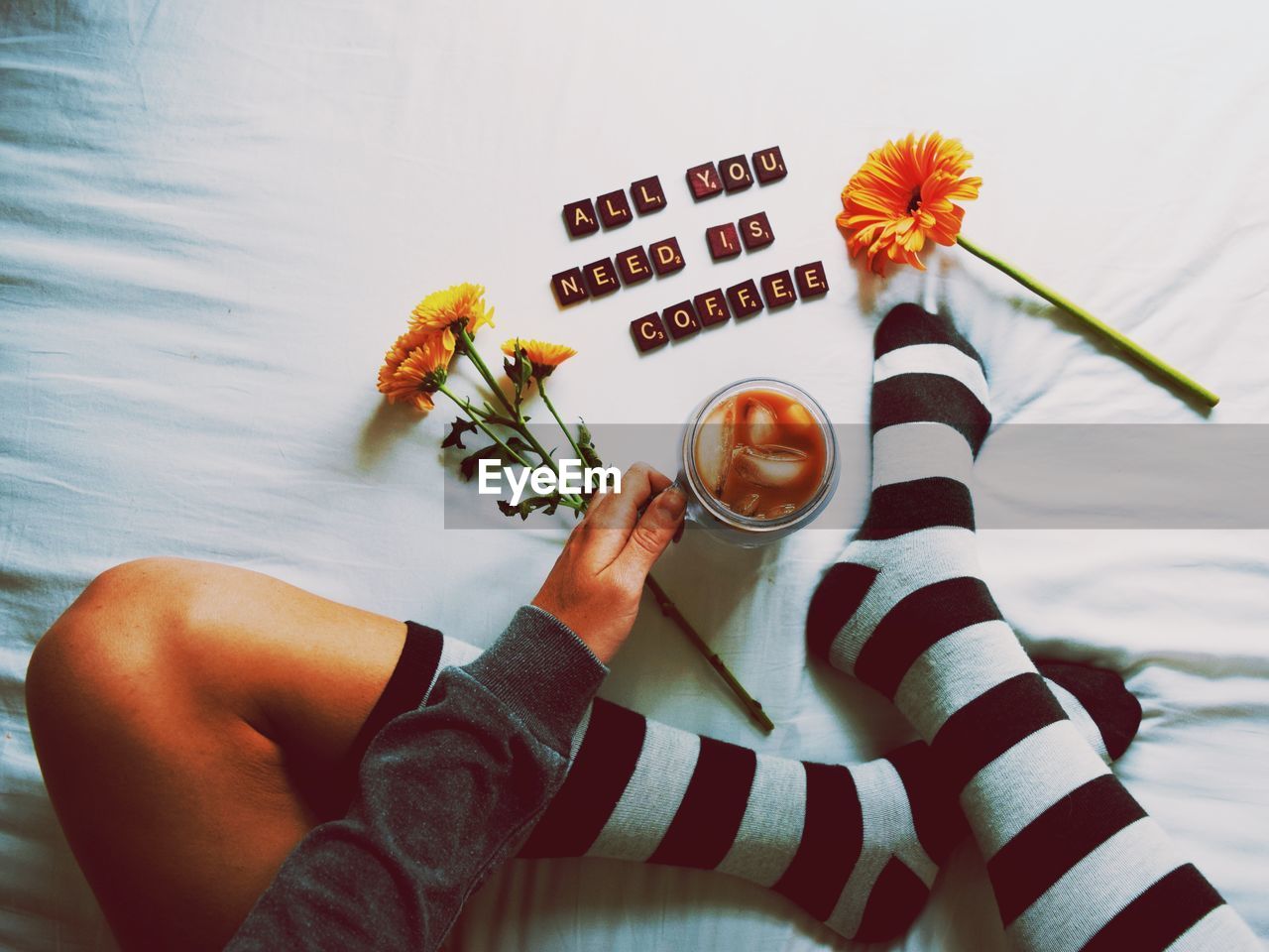 Low section of woman holding coffee cup against text on bed