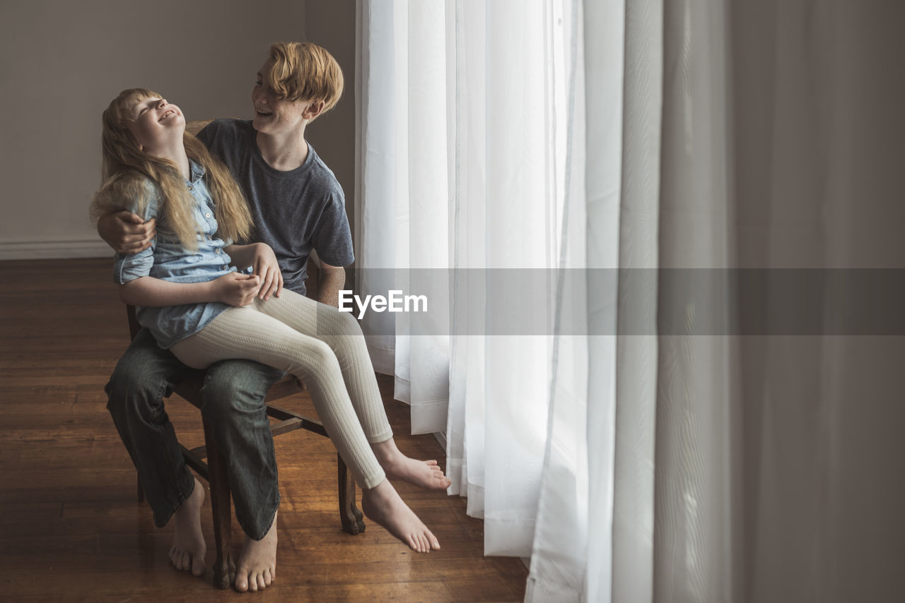 Siblings sitting on chair and laughing in natural light studio