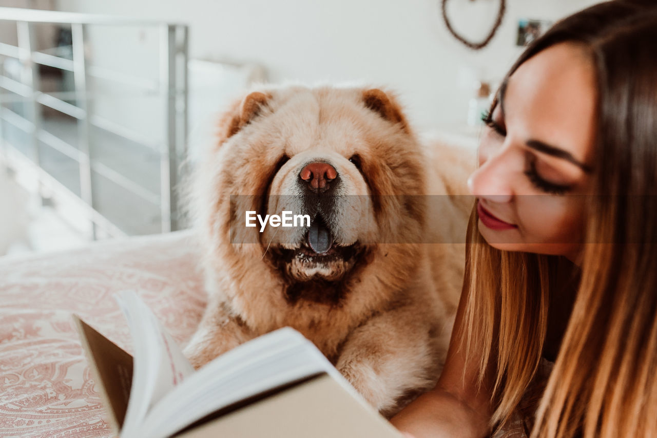 Young woman reading book while lying with dog on bed