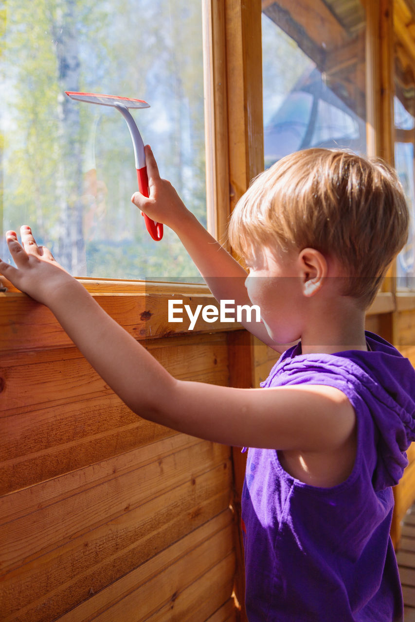 The child washes the windows with a special brush. a child with blond hair