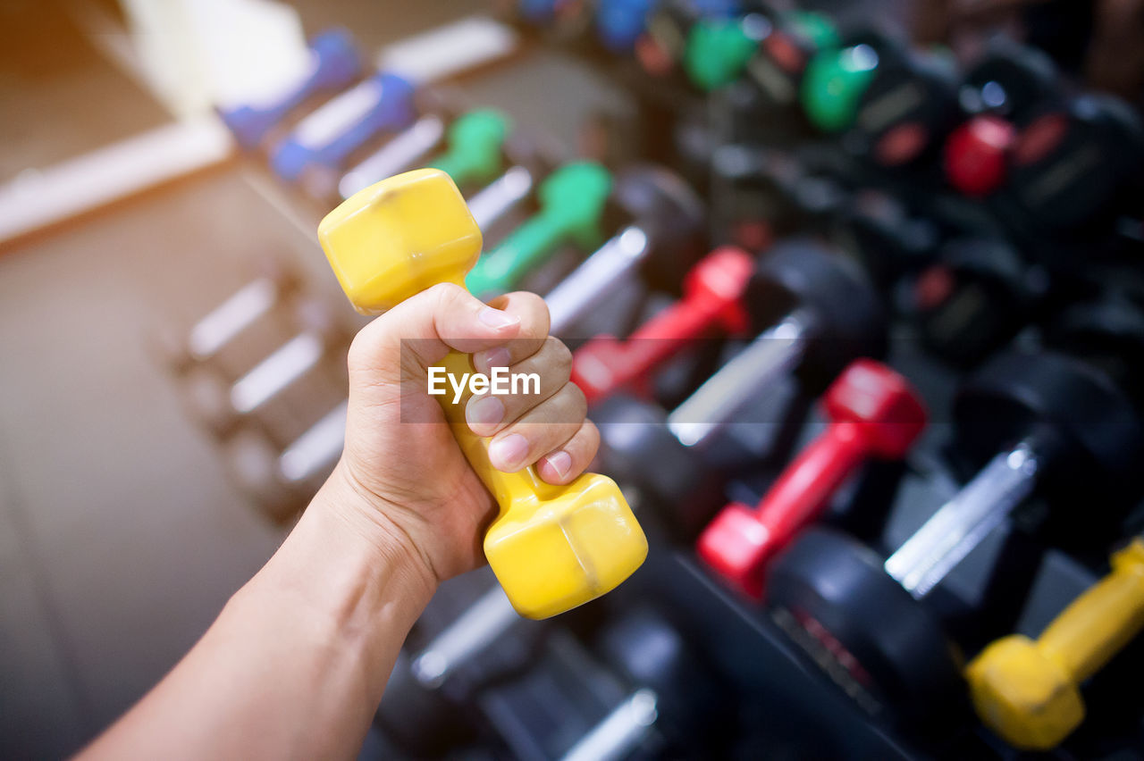 Cropped hand of men lifting dumbbell in gym