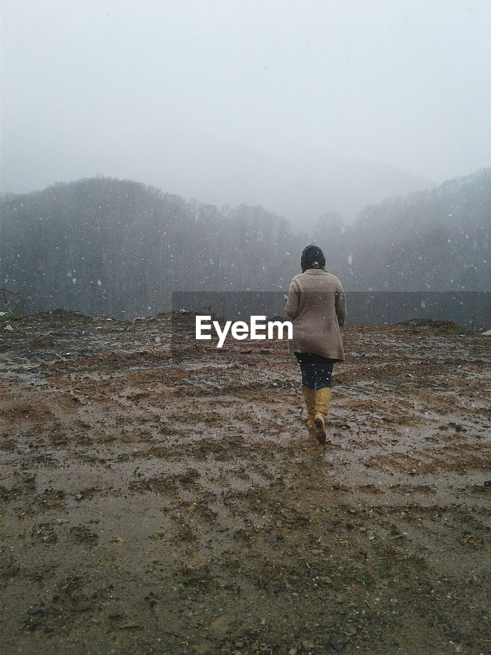Rear view of woman walking on land against mountain during snowfall