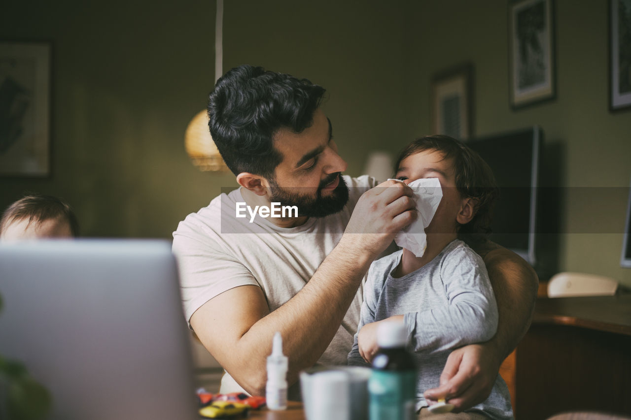 Father blowing nose of son in living room