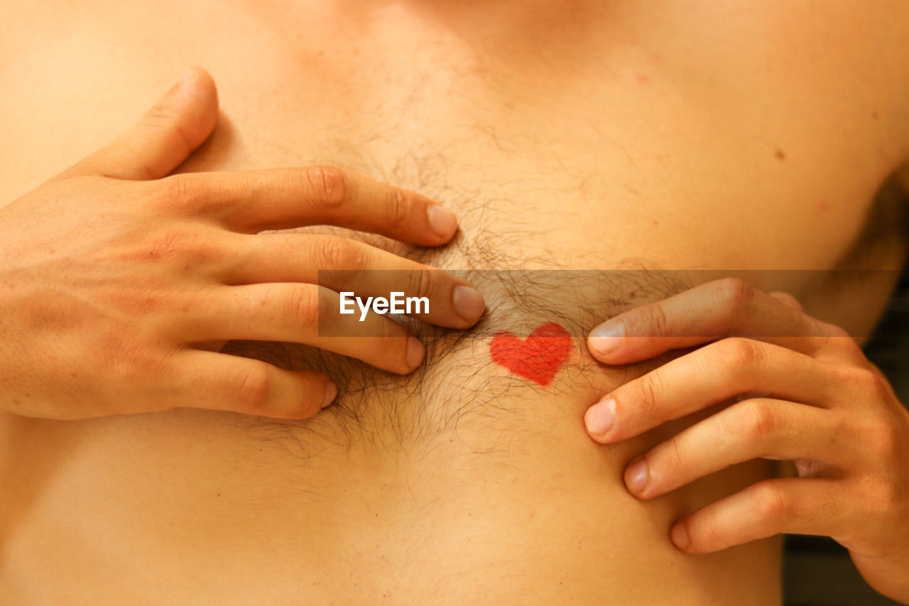 Midsection of person touching red heart shape on chest