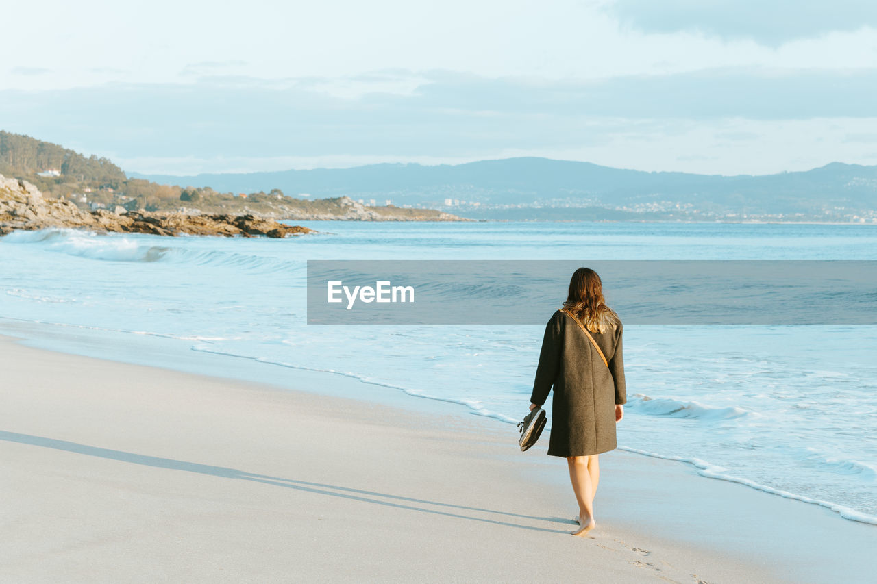 Rear view of woman walking on beach against sky