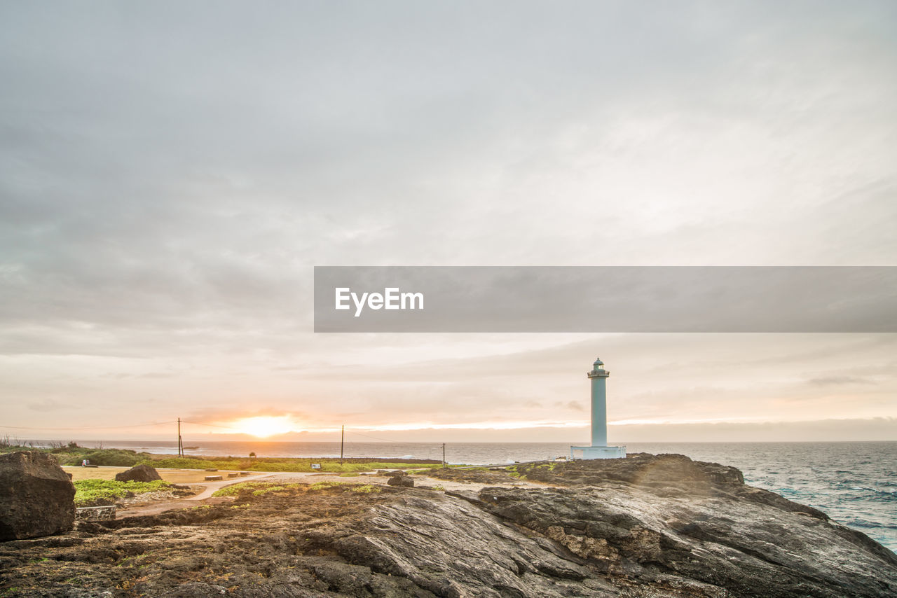 Lighthouse by sea against sky during sunset