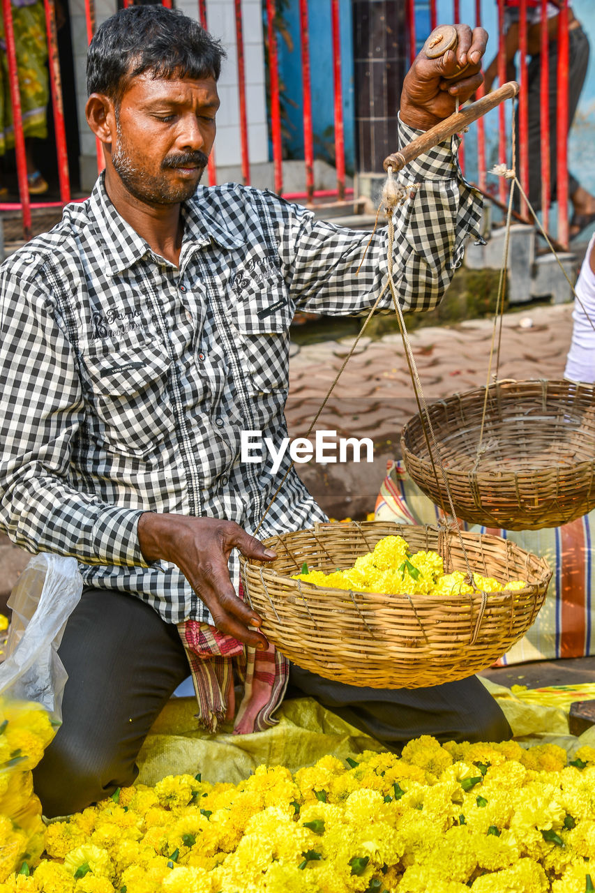 FULL LENGTH OF MAN HOLDING BASKET IN MARKET STALL