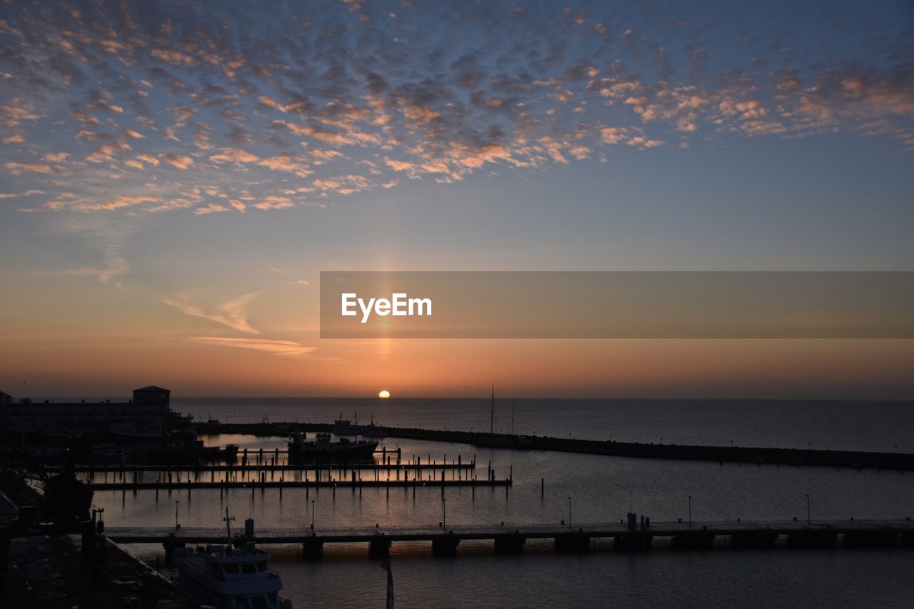 Scenic view of sea against orange sky during sunset seen from harbor