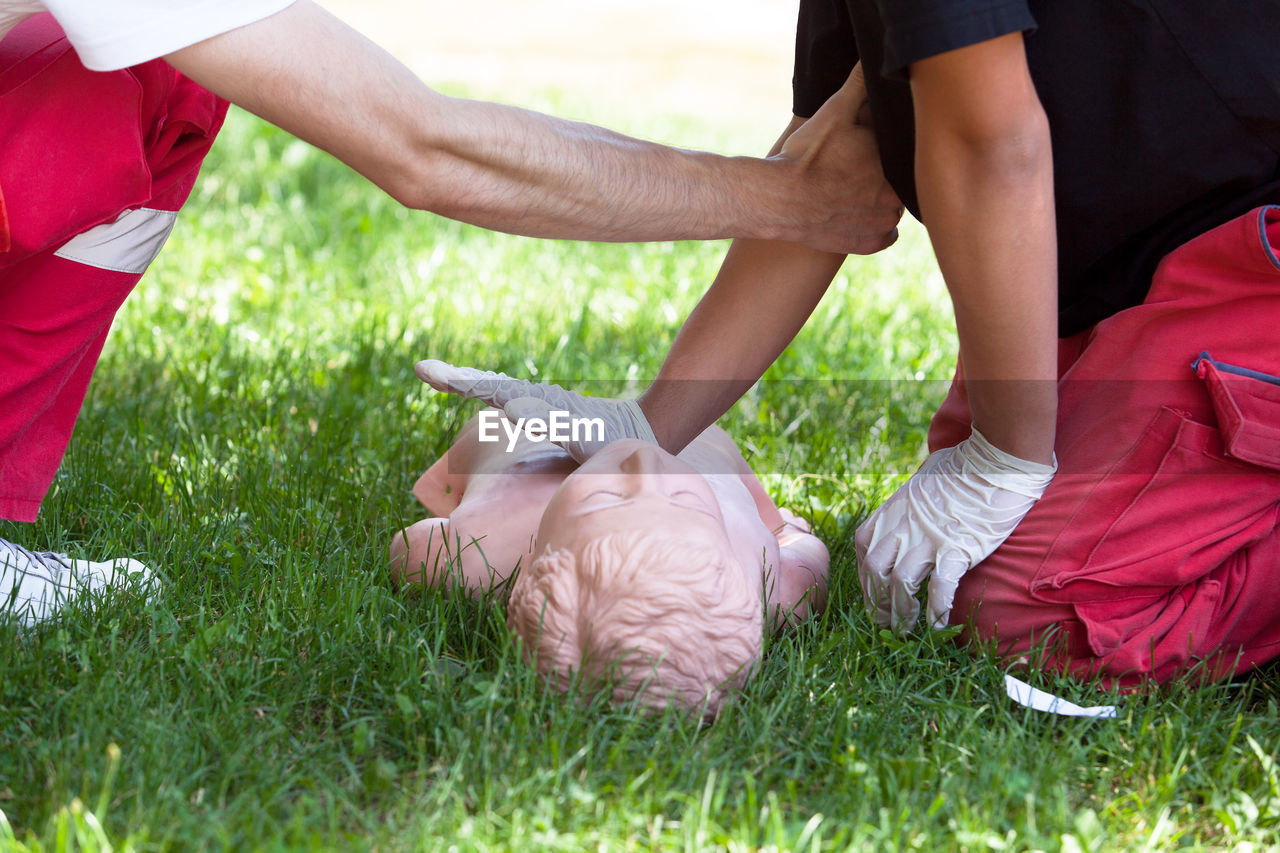 Low section of friends practicing cpr on dummy at grassy field