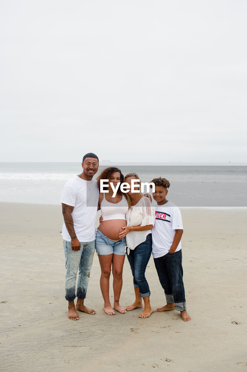 Family posing for maternity photos on beach