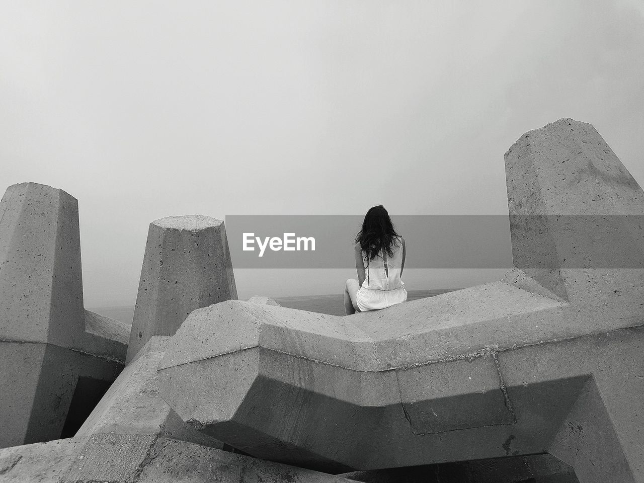 Rear view of woman sitting on tetrapods against sky